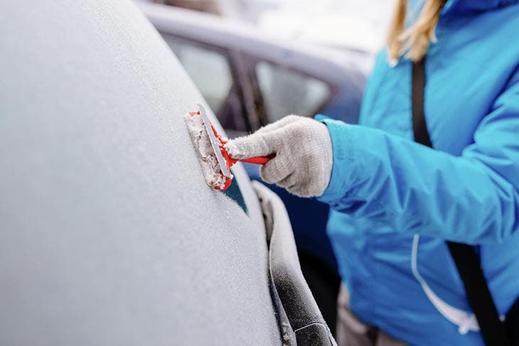 Femme grattant le givre présent sur la lunette arrière de sa voiture